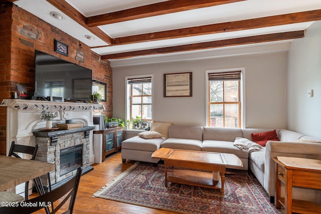 living room with beamed ceiling, a stone fireplace, a healthy amount of sunlight, and light wood-style floors