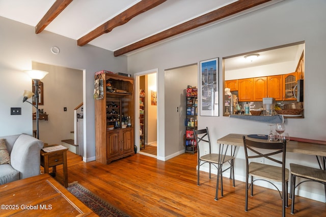 dining room with baseboards, beamed ceiling, stairs, and wood finished floors