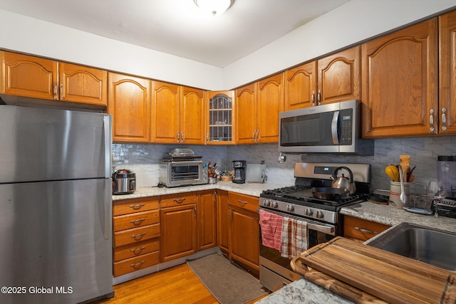 kitchen with brown cabinetry, appliances with stainless steel finishes, a toaster, and backsplash