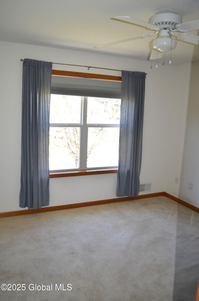 unfurnished room with a ceiling fan, visible vents, carpet, and baseboards