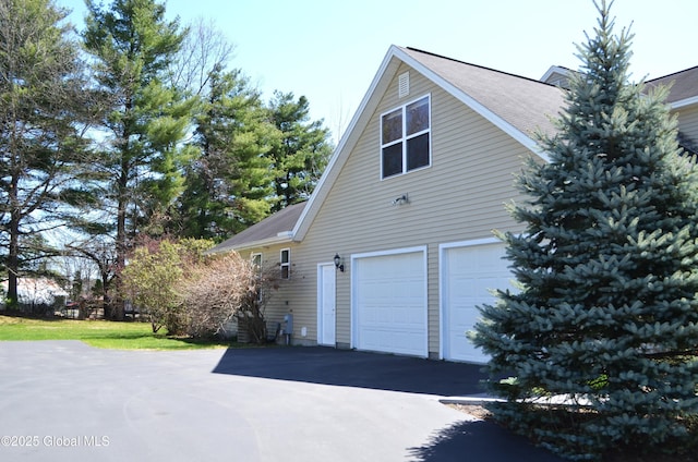 view of side of property with driveway, a shingled roof, and a garage