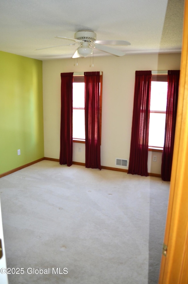 spare room with carpet, visible vents, a ceiling fan, and baseboards