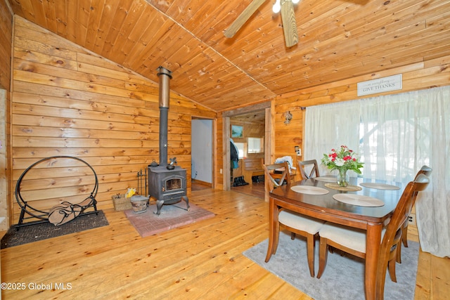 dining room featuring wooden walls, a wood stove, hardwood / wood-style flooring, and lofted ceiling