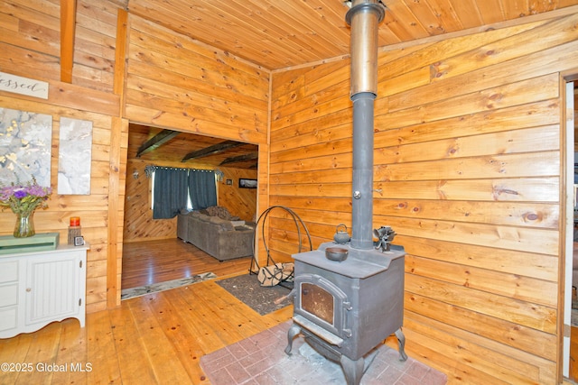 living area featuring wooden walls, wood ceiling, wood-type flooring, and a wood stove