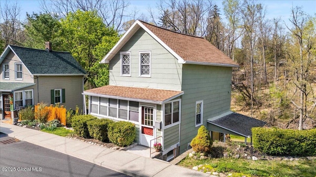view of front of property with roof with shingles, a chimney, and a sunroom