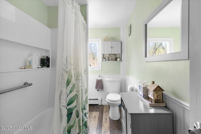 bathroom featuring a wainscoted wall, baseboard heating, wood finished floors, and a wealth of natural light