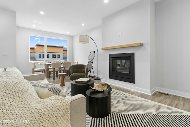 living area featuring a glass covered fireplace, baseboards, recessed lighting, and wood finished floors
