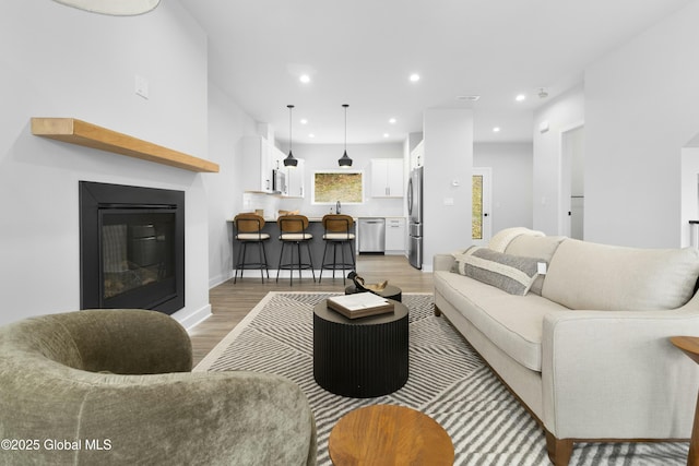 living area with a glass covered fireplace, recessed lighting, and light wood-style flooring