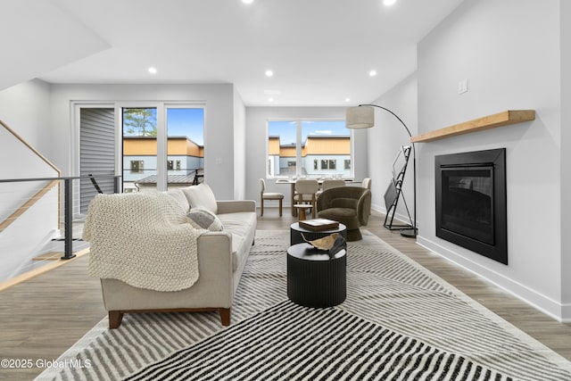 living area with a glass covered fireplace, baseboards, recessed lighting, and wood finished floors