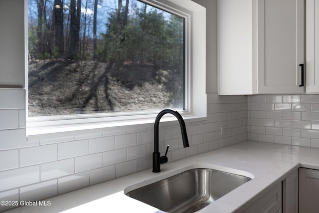 kitchen with a sink, light stone counters, tasteful backsplash, and white cabinets