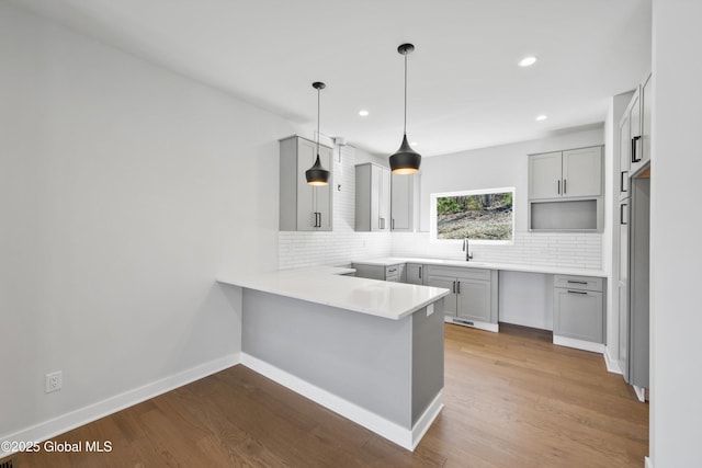kitchen with a peninsula, gray cabinetry, decorative backsplash, and wood finished floors