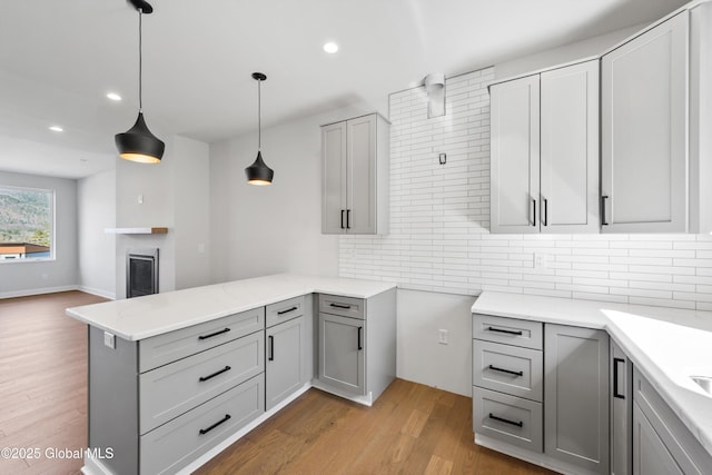 kitchen featuring a peninsula, light wood-style floors, recessed lighting, gray cabinets, and tasteful backsplash