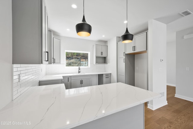 kitchen with visible vents, tasteful backsplash, light stone countertops, wood finished floors, and a sink