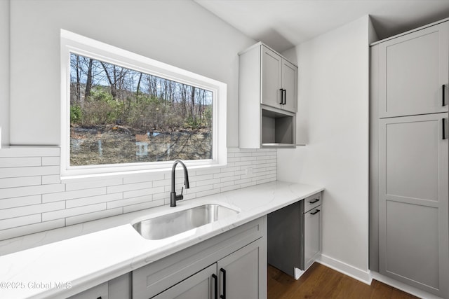 kitchen with dark wood-style flooring, baseboards, light stone counters, a sink, and backsplash