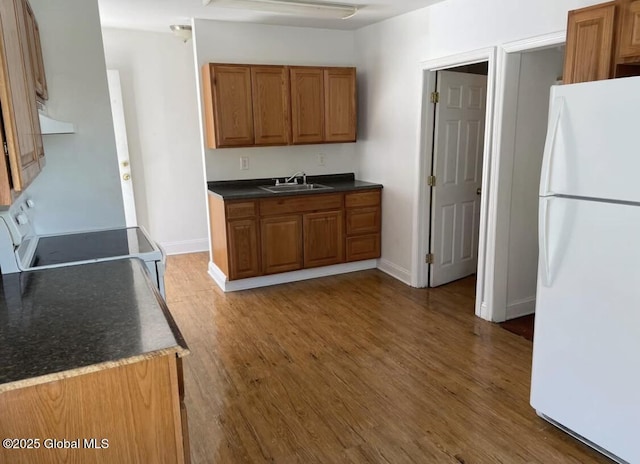 kitchen with wood finished floors, dark countertops, white appliances, brown cabinets, and a sink