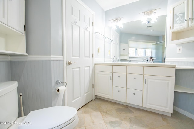 full bath with vanity, a shower with door, wainscoting, and toilet