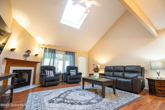 living area featuring wood finished floors, a fireplace, ceiling fan, high vaulted ceiling, and a skylight