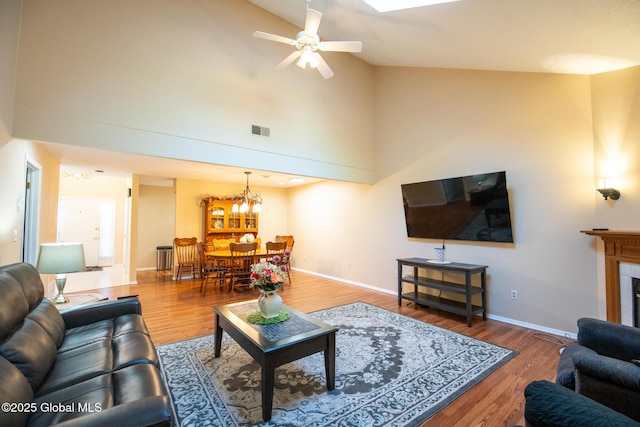 living area with visible vents, wood finished floors, baseboards, high vaulted ceiling, and ceiling fan with notable chandelier