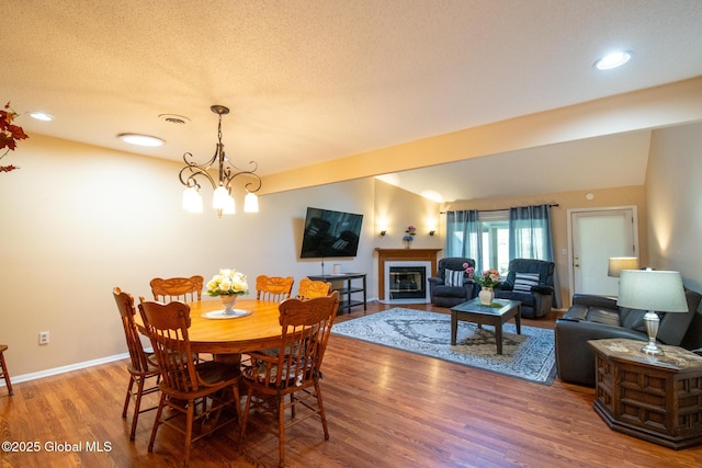 dining area with an inviting chandelier, a glass covered fireplace, baseboards, wood finished floors, and visible vents