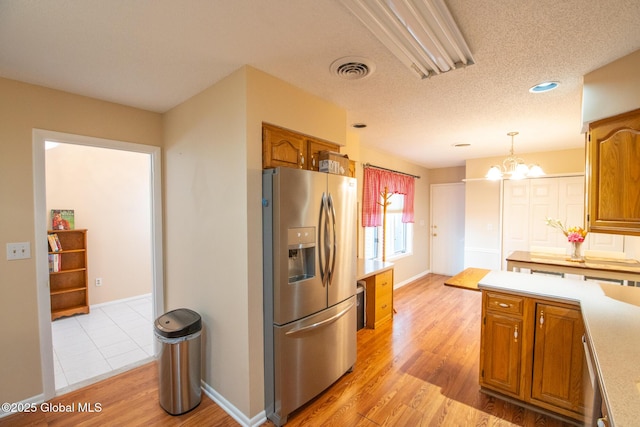kitchen with stainless steel refrigerator with ice dispenser, brown cabinets, light countertops, a chandelier, and light wood-style floors