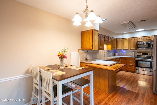 kitchen featuring brown cabinetry, an inviting chandelier, a peninsula, appliances with stainless steel finishes, and backsplash