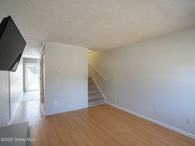 unfurnished living room featuring stairs, a textured ceiling, baseboards, and light wood-type flooring