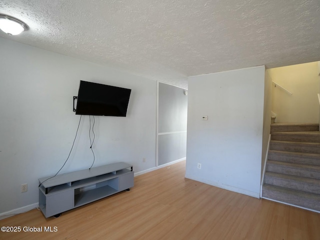 unfurnished living room with stairs, baseboards, a textured ceiling, and wood finished floors