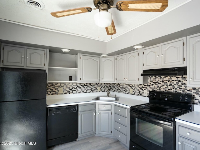 kitchen featuring a sink, tasteful backsplash, under cabinet range hood, visible vents, and black appliances
