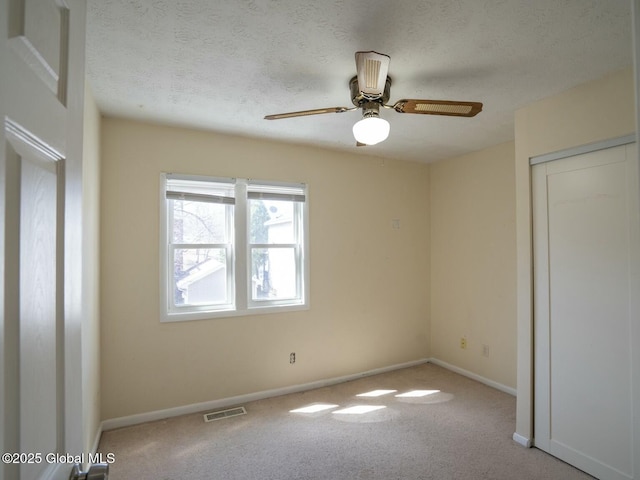 carpeted empty room featuring a ceiling fan, baseboards, visible vents, and a textured ceiling
