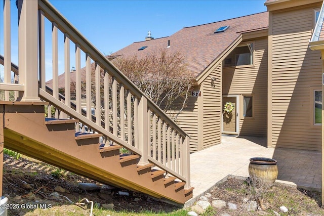 back of property featuring stairway, a patio area, and roof with shingles
