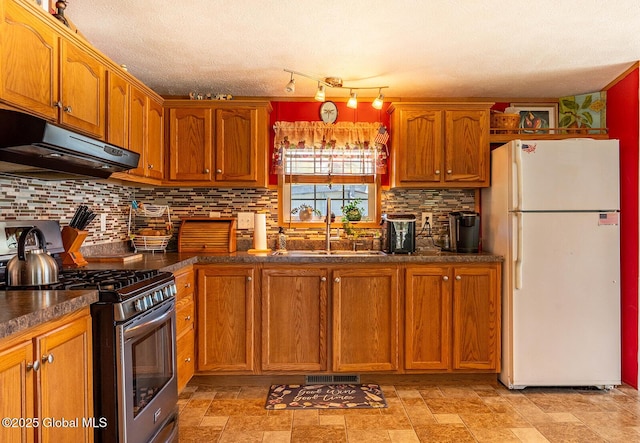kitchen with a sink, freestanding refrigerator, stainless steel range with gas cooktop, under cabinet range hood, and visible vents