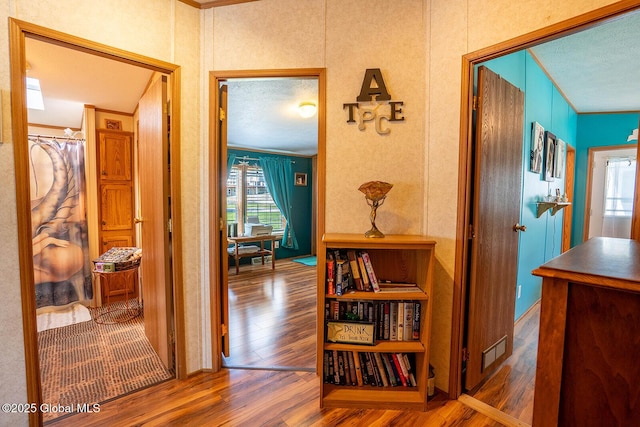 corridor with crown molding, a textured ceiling, visible vents, and wood finished floors