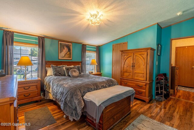 bedroom with crown molding, a textured ceiling, vaulted ceiling, and dark wood-type flooring