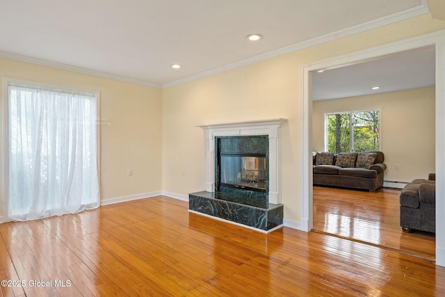 living room featuring a high end fireplace, a baseboard heating unit, hardwood / wood-style flooring, and ornamental molding