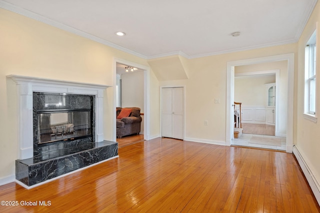 living area with a high end fireplace, baseboard heating, baseboards, light wood finished floors, and ornamental molding