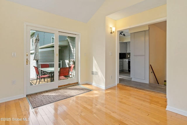 interior space featuring baseboards, vaulted ceiling, light wood-type flooring, and visible vents