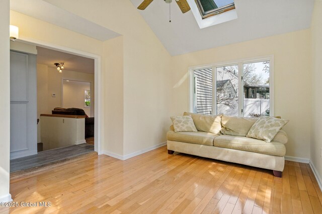 living room with a ceiling fan, a skylight, light wood-type flooring, baseboards, and high vaulted ceiling