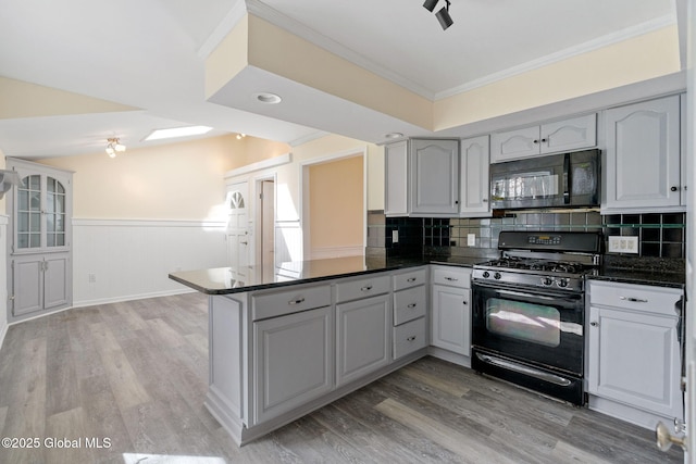 kitchen featuring light wood finished floors, a peninsula, black appliances, and dark countertops