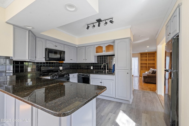 kitchen featuring a peninsula, light wood-style floors, dark stone counters, a sink, and black appliances
