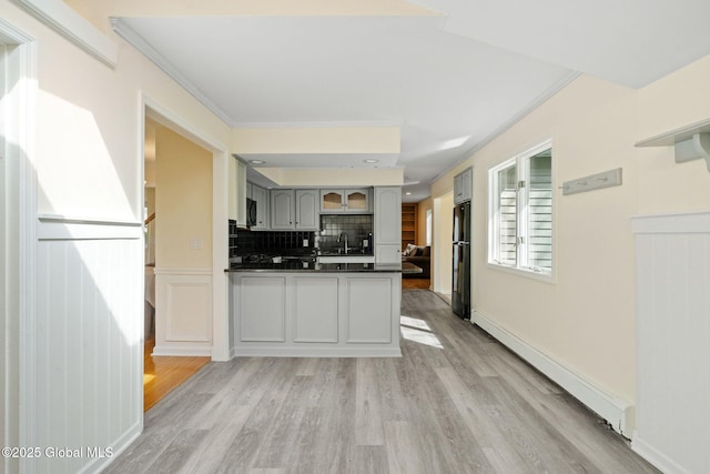 kitchen featuring dark countertops, baseboard heating, a sink, freestanding refrigerator, and light wood finished floors