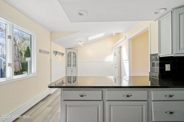 kitchen featuring light wood-style floors, dark stone counters, a peninsula, decorative backsplash, and a baseboard heating unit