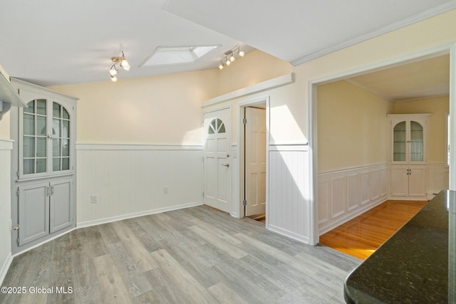 interior space featuring light wood-type flooring, crown molding, a wainscoted wall, and a skylight