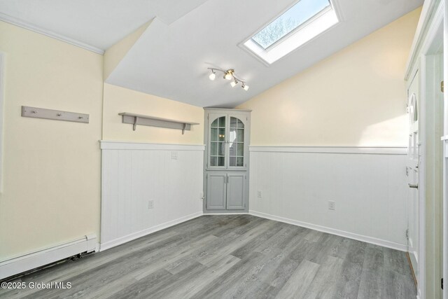 empty room featuring a baseboard heating unit, wainscoting, wood finished floors, and lofted ceiling with skylight