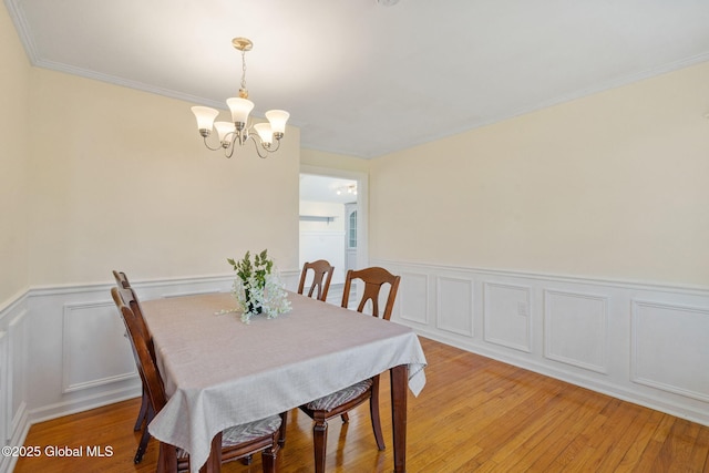 dining area featuring an inviting chandelier, a decorative wall, wainscoting, and light wood-style flooring