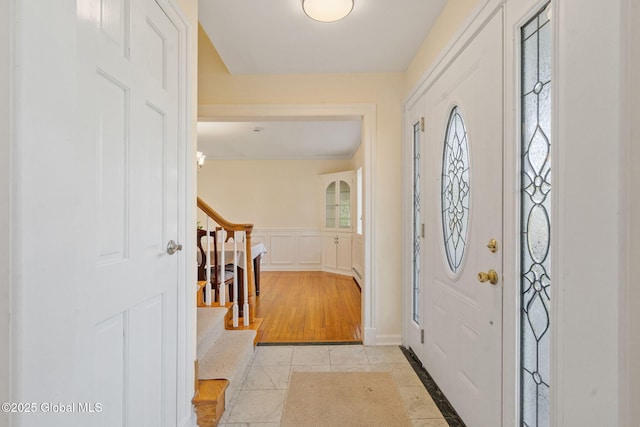 entrance foyer featuring a decorative wall, light tile patterned flooring, stairway, and a wainscoted wall