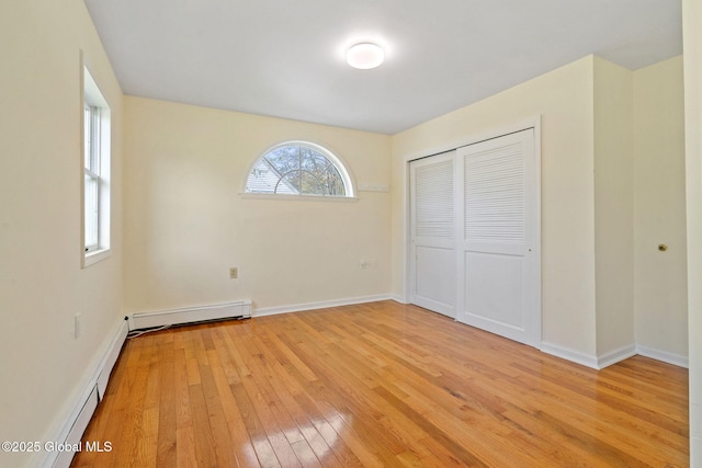 unfurnished bedroom with baseboards, a baseboard radiator, a closet, and light wood-type flooring