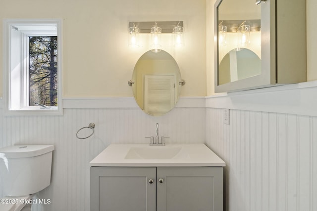 half bathroom with vanity, wainscoting, and toilet
