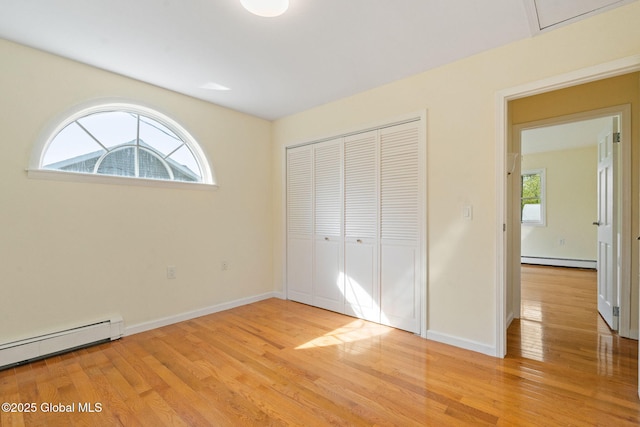 unfurnished bedroom with light wood-style floors, a closet, and a baseboard heating unit
