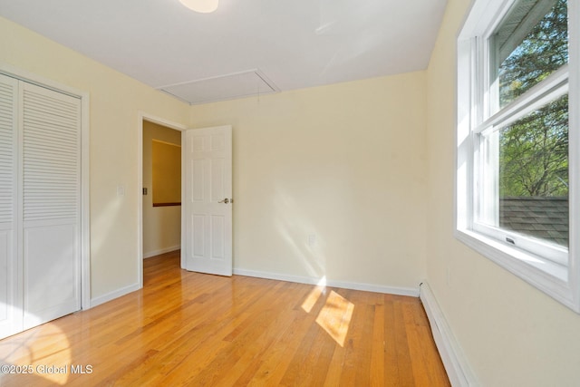 unfurnished bedroom featuring a closet, multiple windows, attic access, and light wood finished floors