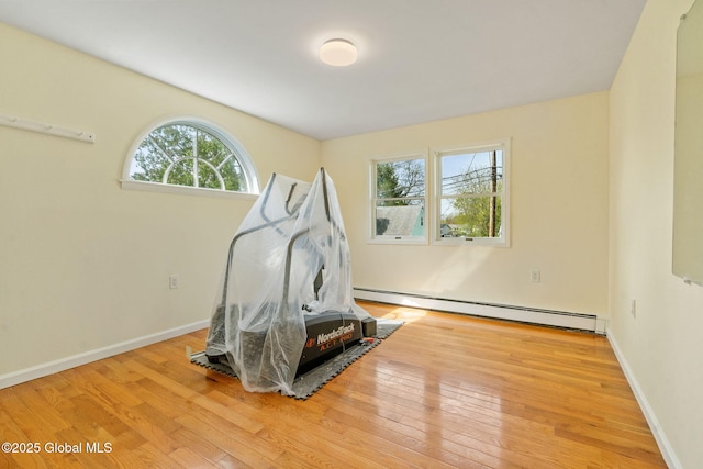 exercise room featuring wood-type flooring, baseboards, and a baseboard heating unit
